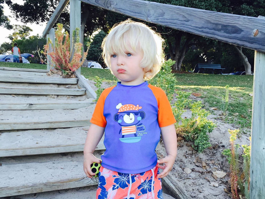 A toddler, a little boy at the beach, with a sad face and long messy scruffy hair